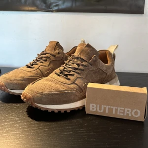 Bruna mockasneakers från Buttero - Snygga sneakers från Buttero i brun mocka med vita detaljer på sulan och grovt mönstrad yttersula. Skorna är i mycket bra skick och i storlek 42. Det tillkommer även extra skosnören för dig som beställer! Skriv vid fler frågor 
