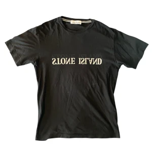 Svart Stone Island t-shirt med tryck - Svart t-shirt från Stone Island med klassiskt rund halsringning och vit spegelvänd logga på bröstet. Står storlek L på lappen men sitter som M