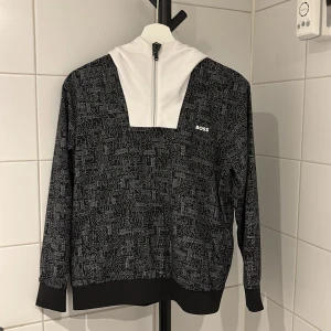 BOSS tracksuit  - Snygg hoodie från BOSS i svart med vitt abstrakt mönster och vit huva. Tröjan har half zip framtill, långa ärmar och ribbade muddar. Perfekt för dig som gillar streetstyle och vill sticka ut med en unik design. Inuti är det skönt sportmaterial. Tillkommer feta shorts. Tröjan är aldrig använd medans shortsen är använda fåtals gånger allt är som nytt. Köptes för 3199kr limiterat. Vill du bara köpa tröjan funkar det samma med shortsen! Kan tänkas byta mot ett annat plagg. Pris kan diskuteras!!!!