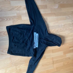 Svart hoodie med citattryck - Svart hoodie med huva och snörning. På bröstet finns ett stort vitt tryck med texten 'Vinner vi inte idag spränger vi ishallen.' av Christoffer S. Perfekt för dig som gillar statement-plagg och sportig stil.