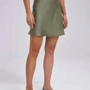 Olivgrön satin kortkjol - Snygg olivgrön kortkjol i glansigt satinmaterial. Kjolen har en lätt A-linjeform och faller mjukt, perfekt för en chill och trendig look. Enkel att matcha med både sneakers och boots.