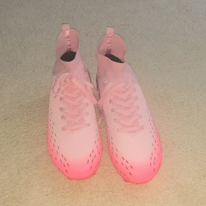 CR7 rosa fotbollsskor med snörning - Snygga fotbollsskor i rosa med svarta CR7-detaljer och coola svarta mönster. Skorna har snörning, högre strumpliknande skaft och dobbar för gräsplan. Tillverkade i syntetmaterial för lätt känsla och bra passform. Helt ny.