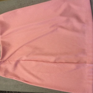 Rosa ribbad kortkjol med slits - Supersöt rosa kortkjol med tunna horisontella ränder och en liten slits på sidan. Kjolen är ribbad och har en tight passform som framhäver siluetten. Perfekt för dig som vill ha en enkel men ändå trendig look.