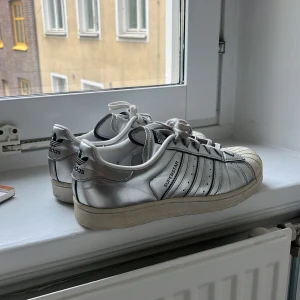 Adidas Superstar silver sneakers  - Snygga Adidas Superstar sneakers i metallic silver. Finns defekter men är i ett bra skick! Skosnörena är lite smutsiga men går att bytas ut. 