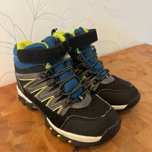 Svarta och blå kängor  - Tuffa kängor i svart och blått med gröna detaljer och grov sula. Skorna har snörning med reflexdetaljer, kardborreband upptill och vadderad insida i gult. Storlek 32-33