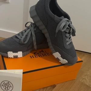 Grå sneakers  - Snygga grå sneakers  med cool ribbad sula i grått och vitt. Ovandelen är i mesh och mocka för en modern vibe. Skorna har snörning och en unik design med H-detalj på sulan. Perfekta för dig som vill sticka ut med lyxig streetstyle.