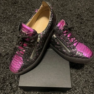 Giuseppe Zanotti sneakers i svart och lila - Giuseppe Zanotti sneakers – knappt använda  Säljer dessa lyxiga sneakers från Giuseppe Zanotti i svart och metallic-lila med reptilmönster. Superunika med dragkedjor, skinnfoder och chunky sula. Använda endast 2 gånger – i toppskick!   Originalkartong finns  Storlek: 44  Perfekta för dig som vill sticka ut med stil! Pris kan diskuteras vid snabb affär 