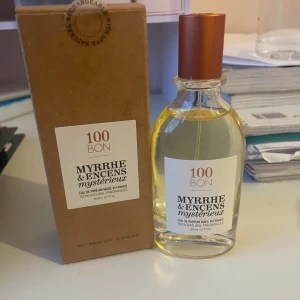 100BON Myrrhe & Encens Mystérieux parfym - Parfymen Myrrhe & Encens Mystérieux från 100BON kommer i en stilren, genomskinlig glasflaska med kopparfärgad kork och vit etikett. Doften är tillverkad i Frankrike och innehåller 100% naturliga ingredienser. Flaskan rymmer 50 ml och levereras i en brun kartong.