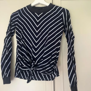 Randig långärmad topp från Zara Basic - Snygg långärmad topp från Zara Basic i marinblått med vita ränder. Tröjan har ett coolt knyt framtill och rund halsringning. Perfekt för dig som gillar en stilren men ändå trendig look. Materialet är mjukt och stretchigt för extra komfort.