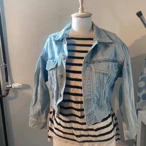 Ljusblå croppad jeansjacka - Snygg ljusblå jeansjacka i croppad modell med klassisk krage och knappar framtill. Jackan har två bröstfickor med lock och långa ärmar. Perfekt för dig som vill ha en chill och trendig look till våren eller sommaren.