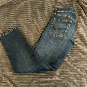 Jack&jones jeans - Snygga blå jeans från Slim Glenn i storlek 31/30. Jeansen har en slim passform, klassiska bakfickor med diskret broderi och slitna detaljer för en cool look. Perfekta för dig som gillar en smalare siluett och vill ha ett par stilrena jeans i garderoben.