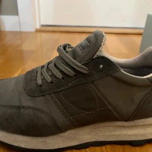 Grå Philippe Model sneakers i mocka och skinn - Snygga grå sneakers från Philippe Model med ovandel i mocka och skinn, coola detaljer och klassisk snörning. Skorna har en platt sula och rund tå, perfekt för en stilren och avslappnad look. Passar dig som gillar exklusiva och trendiga sneakers. Använda få gånger men blev för små. Pris kan diskuteras.