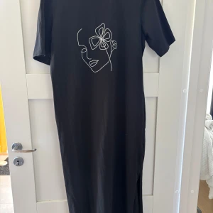 Svart långklänning från iDEA - Svart långklänning från iDEA med kort ärm. Rak passform och mjukt bomullstyg gör den både bekväm och stilren.