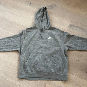 Grå Nike hoodie med huva XL - Aldrig använd, NYSKICK! Säljer en grå hoodie från Nike i storlek XL. Tröjan har klassisk huva med snörning, stor magficka och Nike-logga broderad på bröstet. Perfekt för chill dagar eller när du vill ha en enkel och stilren look.
