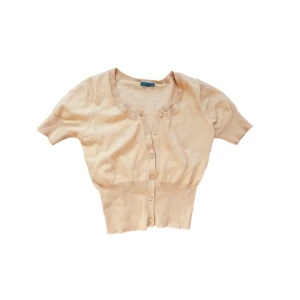 Gul kortärmad kofta med knappar - Supersöt gul kofta med korta ärmar och knappar framtill. Modellen är croppad med bred ribbad midja som ger en snygg siluett. Perfekt att slänga över ett linne eller klänning för en chill look. Färgen är lite gulare i verkligheten, men jag lyckades inte gå de på bild!