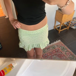 Ljusgrön blommig volangkjol - Supersöt ljusgrön kortkjol med småblommigt mönster och volang längst ner. Kjolen har en tight passform upptill och är perfekt för varma dagar. Den är gjord i ett mjukt och lätt material som känns skönt mot huden.