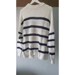 Randig stickad tröja från 157 storlek XS - Vit och marinblå stickad tröja från 157 i storlek XS. Tröjan har breda horisontella ränder, ribbade muddar och en rund halsringning. Perfekt för dig som gillar en klassisk och chill stil med lite oversized känsla.