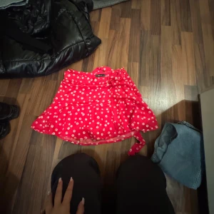 Röd blommig omlottkjol från Newyork - Superfin röd kortkjol från Newyork med vita blommor och omlottmodell. Kjolen har en söt knyt-detalj i midjan och är perfekt för dig som gillar färg och mönster. Lätt och flowy känsla, passar perfekt till sneakers eller sandaler.