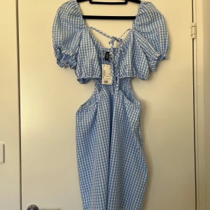 Ny blåvit rutig klänning H&M strl 44 - Ny söt blåvit rutig klänning från H&M med puffärmar, cut-out i midjan och knytning fram.