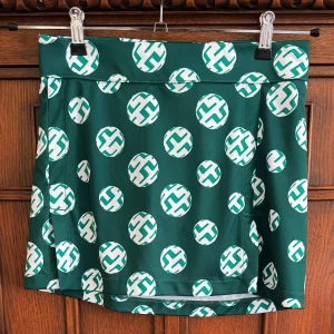 Grön golfkjol J.Lindeberg S - Grön golfkjol från J.Lindeberg med vitt och grönt cirkelmönster. Modellen heter Amelie Print Skirt och är tillverkad i stretchigt material med 92% polyester och 8% elastan. Kjolen har en sportig vibe och är perfekt för dig som gillar att sticka ut.