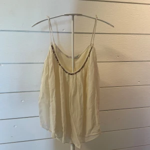 Ljusbeige linnetopp från Zara Basic - Supersöt ljusbeige linnetopp från Zara Basic med tunna axelband och flowig, luftig passform. Toppen har en snygg detalj med små pärlor längs urringningen och är tillverkad i ett tunt, skirt material som känns perfekt för varma dagar.