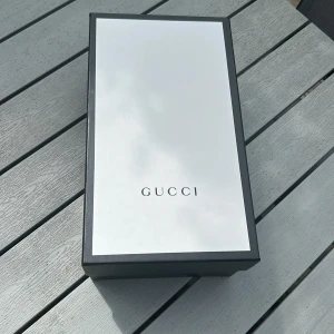 Gucci ace skor - Snygga svarta Gucci sneakers med klassisk röd och marinblå rand på sidan. Skorna har snörning, vit platt sula och diskret GG-mönster i tyget. Kommer med originalbox och dustbags. Perfekta för dig som vill ha en lyxig och stilren look.