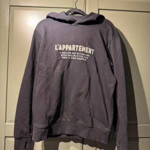 Svart hoodie från Mango med tryck - Svart hoodie från Mango med texten 'L'APPARTEMENT' tryckt på ryggen. Klassisk modell med huva och långa ärmar. Tillverkad i mjuk bomull, perfekt för en chill och avslappnad stil.