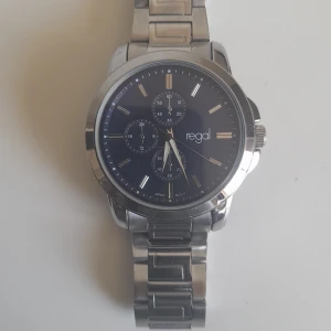 Regal herrklocka i silver med blå urtavla - Stilren klocka från Regal med blå urtavla och flera små urtavlor för extra funktioner. Boett och länk i silverfärgat rostfritt stål. Klassisk rund form och tydliga indexmarkeringar. Perfekt accessoar för dig som gillar en clean och modern look.