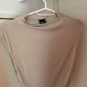 Beige ärmlös topp från Gina Tricot - Säljer en stilren beige ärmlös topp från Gina Tricot. Toppen har en enkel, rak passform med breda axlar och rund halsringning. Perfekt att matcha med jeans eller kjol för en clean look.