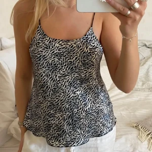 Zebramönstrad linnetopp med tunna band - Snygg linnetopp med zebramönster i svart och vitt. Toppen har tunna, justerbara axelband och en lätt utsvängd passform. Perfekt för varma dagar och ger en cool vibe till din outfit. Materialet känns lätt och luftigt mot huden.