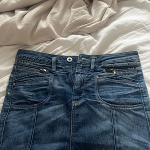 Blå jeans från G-Star RAW med dragkedjor - Snygga blå jeans från G-Star RAW med coola detaljer som dragkedja på fickan och broderad logga. Klassisk femficksmodell med kontrastsömmar och patch bak i midjan. Jeansen har en normal passform och är tillverkade i slitstarkt denimtyg.