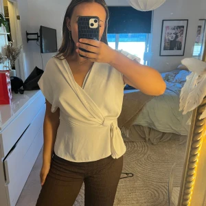 Vit omlottopp med knyt i midjan - Säljer en vit omlottopp med knyt i midjan och v-ringad hals.. Perfekt att styla med jeans eller kjol. Tröjan har spruckit lite i armvecket men de är inget man tänker på och de går lätt att sy igen💕