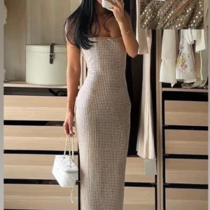 Glittrig långklänning i beige och silver - Supersnygg långklänning i beige med glittriga silverpaljetter över hela klänningen. Figurnära passform, ärmlös och med rak urringning. Helt ny med prislapp, nypris ca.  2.000. 