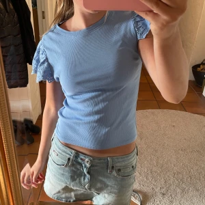 Blå topp med spetsärmar från Gina Tricot - Supersöt ljusblå topp från Gina Tricot med ribbad struktur och korta volangärmar i broderad spets. Toppen är figurnära och har rund halsringning. Perfekt för dig som vill ha en feminin och trendig look. Jag är 165cm lång, så den passar även på dig som är under 170 cm☺️