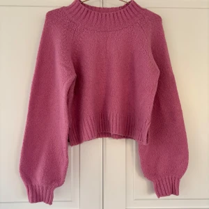 Rosa stickad tröja med ballongärmar - Superfin rosa stickad tröja med bred ribbad krage och muddar från Gina Tricot. Tröjan har ballongärmar och är något croppad i modellen, vilket ger en trendig och avslappnad look. Perfekt att styla med jeans eller kjol för en cool vardagsoutfit eller för en sen sommarkväll!