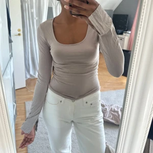 Beige långärmad topp  - Supersnygg beige långärmad topp från Gina Tricot med tight passform och rundad, djup urringning. Toppens material är mjukt och stretchigt och ärmarna har en slitsdetalj vid handleden. Endast testad! 