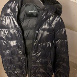 Svart dunjacka Peak Performance - Snygg svart dunjacka från Peak Performance som inte finns att köpa längre.Jackan har en glansig look med huva och dragkedja framtill och Peak Performance-logga på ärmen. Perfekt för kalla dagar och riktigt skön att bära. Nypris:2300. Finns inte att köpa längre. Billigare vid snabb affär