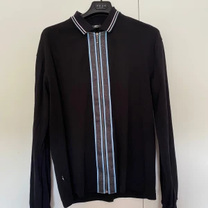 Svart tröja från sweet sktbs - Svart långärmad pikétröja från Sweet SKTBS med dragkedja framtill och mönstrad blå och grå rand längs dragkedjan. Fint skick och är i storlek Medium.