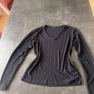 Svart ribbad långärmad tröja 157 - Svart långärmad tröja från 157 i ribbat material. Tröjan har v-ringning och en slim passform som sitter snyggt på kroppen. Perfekt att styla med jeans eller kjol för en clean look.