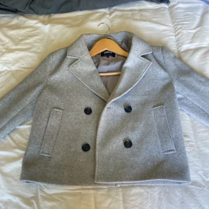 Grå skepparkavaj från ONLY XS - Snygg grå skepparkavaj från ONLY i klassisk modell med dubbelknäppning och stora svarta knappar. Jackan har bred krage, raka fickor och är helfodrad. Perfekt för dig som gillar stilren och tidlös look. (Köpt för 800kr)