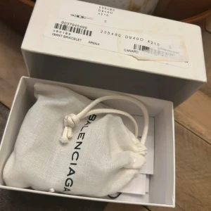 Balenciaga svart läderarmband - Coolt svart armband från Balenciaga i äkta läder med bred design och silverfärgade detaljer. Armbandet har en snygg spänne framtill och präglad logga på baksidan. Kommer med originalpåse och box – perfekt för dig som gillar statement-accessoarer.