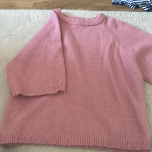 Rosa stickad tröja med trekvartsärm - Mysig rosa stickad tröja med trekvartsärmar och rund halsringning. Tröjan har en avslappnad passform och ribbade muddar vid ärmslut och nederkant. Perfekt för lager-på-lager och chill dagar.