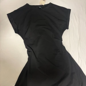 Svart och beige t-shirtklänning - Enkel svart t-shirtklänning med rund halsringning och korta ärmar. Klänningen har en avslappnad passform och är gjord i mjuk bomull, scrunchad i midjan. Likadan även i Beige!