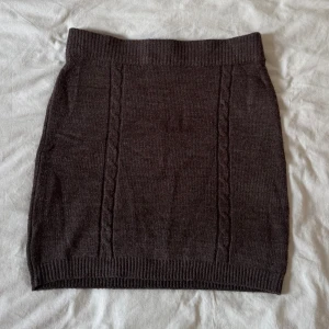Mörkbrun stickad kortkjol - Mysig mörkbrun stickad kortkjol med ribbad midja och nederkant. Kjolen har diskreta kabelstickade detaljer framtill. Från Gina tricot.