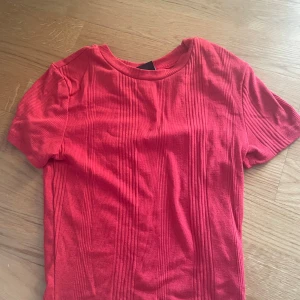 Röd ribbad t-shirt från Gina Tricot - Snygg röd t-shirt från Gina Tricot i storlek S. T-shirten har korta ärmar och ett ribbat mönster med vertikala ränder som ger en cool struktur. Perfekt till jeans eller kjol för en enkel men trendig look.