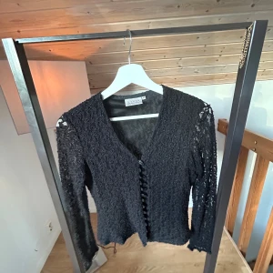 Svart spetskofta med knappar - Säljer en svart kofta från woman med v-ringning och dekorativa knappar framtill. Koftan är i spetsmaterial med långärmade ärmar och har en feminin, elegant look. Perfekt för dig som gillar detaljer och vill sticka ut lite extra.