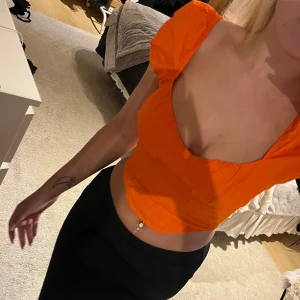 Orange croppad topp med puffärm - Säljer en orange croppad topp med korta puffärmar och fyrkantig urringning. Toppen har smockad rygg och sitter tight över kroppen för en snygg siluett. Perfekt för dig som vill sticka ut med färg och trendig passform. Storlek 36 men sitter ganska tight för mig som vanligtvis bär xs. Endast använd ett par gånger. 