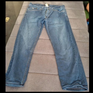 Blå jeans från Archiles, storlek 36 - Säljer ett par klassiska blå jeans från Archiles i storlek 36. Jeansen är tillverkade i 100% bomull och har en rak passform med snygga kontrastsömmar och fem fickor. Perfekta för dig som gillar en tidlös denimlook.