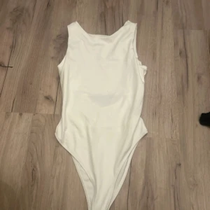 Vit ärmlös bodysuit i stretchigt tyg - Säljer en stilren vit bodysuit med ärmlös design och rund halsringning. Bodyn har en öppen rygg!