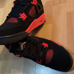 Nike Air Jordan 4 Svart/Röd - Grymma Nike Air Jordan 4 sneakers i svart och rött med coola meshdetaljer och klassisk Jumpman-logga på plösen. Skorna har snörning, platt sula och är tillverkade i syntet och mocka. Perfekta för dig som vill sticka ut med en ikonisk streetstyle.